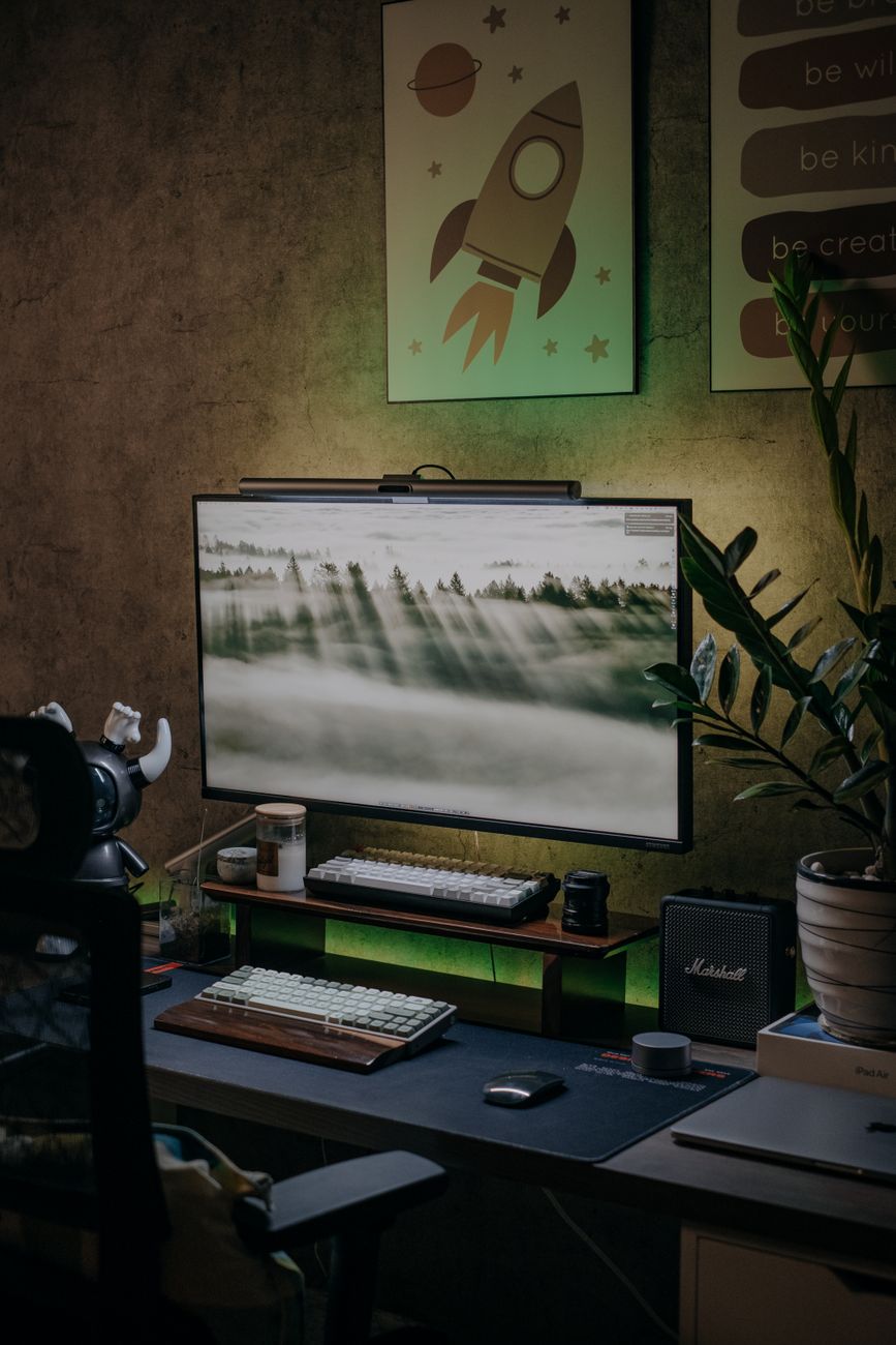 A cozy home office with a modern desk setup, featuring a desktop computer, green accents, and motivational posters.