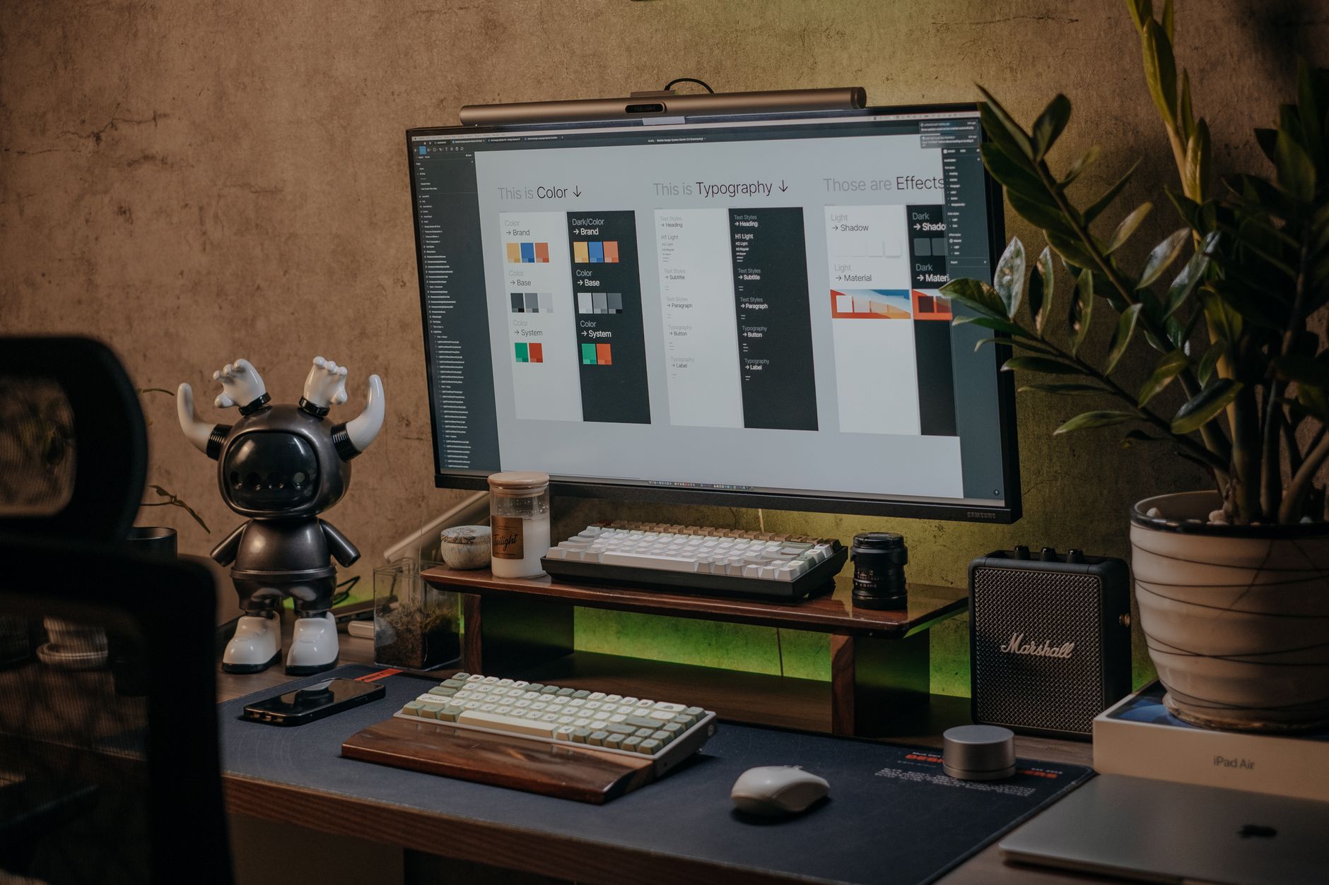 A minimalist desk setup featuring a large monitor, keyboard, houseplant, and stylish decor.