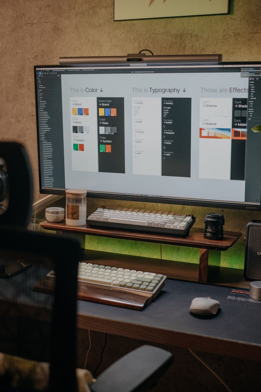 A stylish home office featuring a large monitor displaying a design layout with a sleek keyboard and desk accessories.