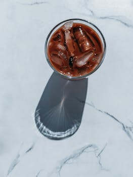 A top view of an iced coffee with ice cubes casting a long shadow on a marble surface.