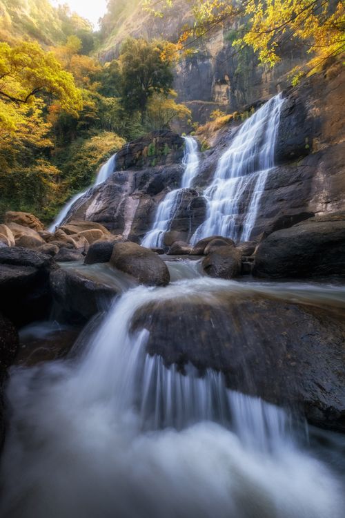 Free A picturesque waterfall cascading down rocks in a vibrant autumn forest in West Java, Indonesia. Stock Photo