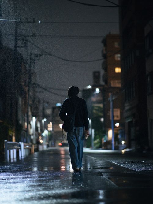 Free A person walking down an illuminated urban street at night in the rain. Stock Photo