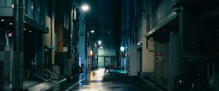 Nighttime city street with a lone pedestrian crossing, illuminated by streetlights.
