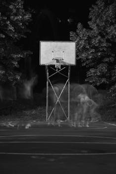 Black and white photo capturing blurred motion of basketball players at a night court