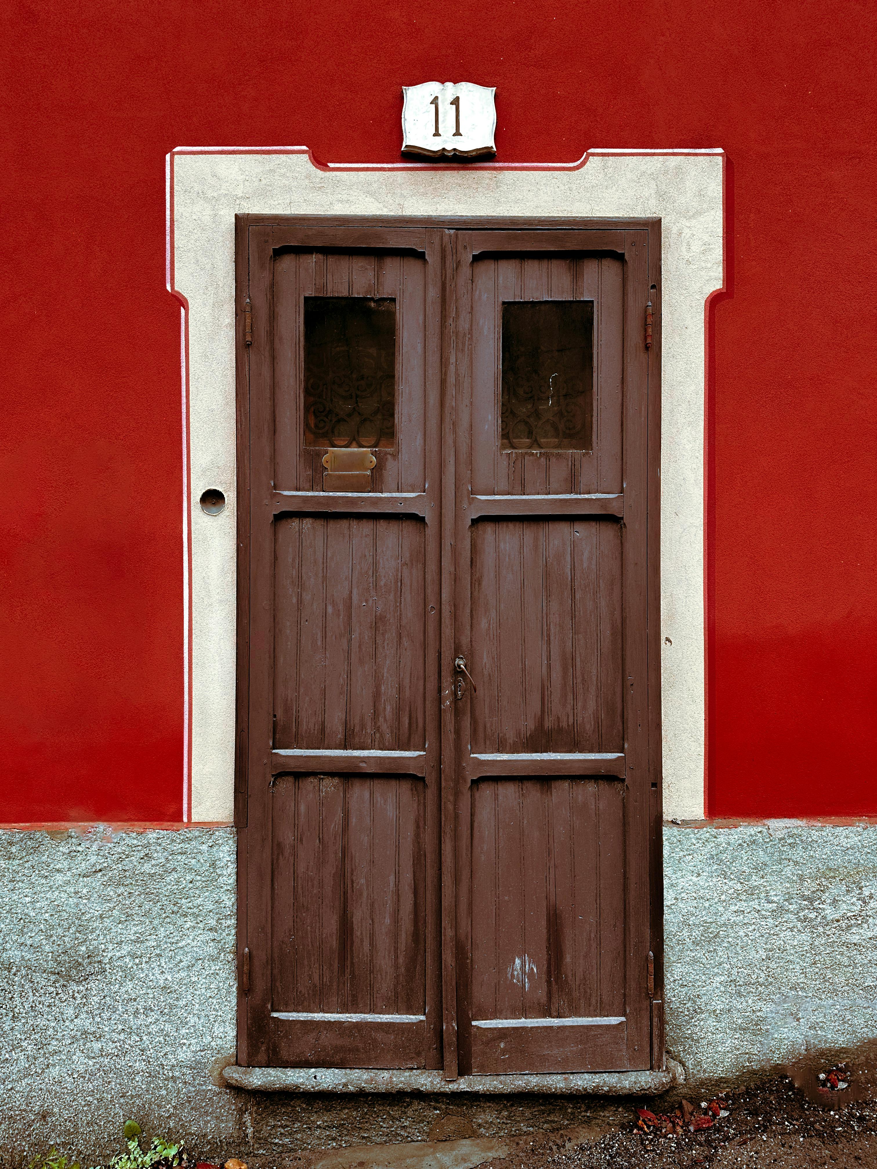 A rustic wooden door with a vibrant red wall background and number 11 above it.