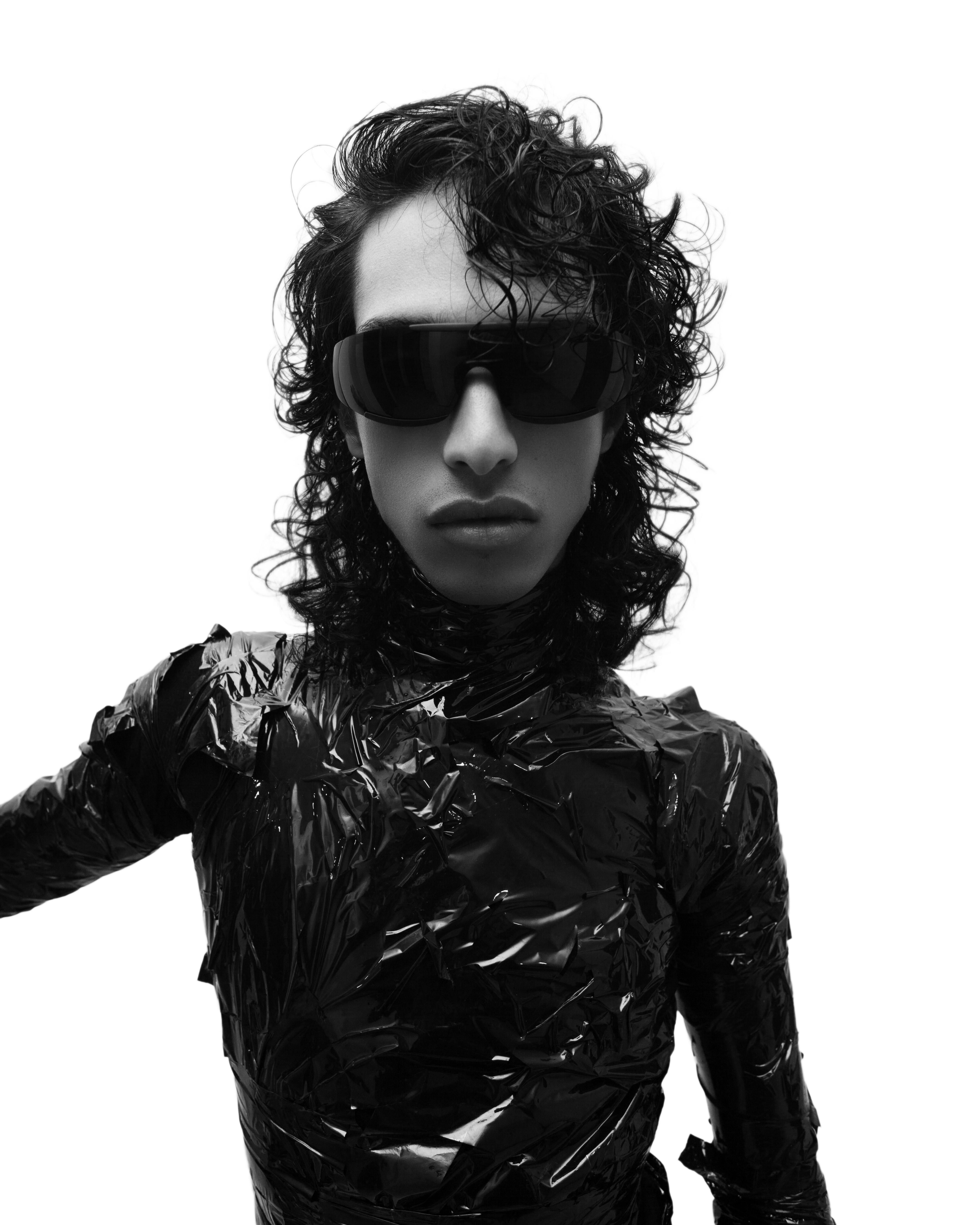 Chic portrait of a young man in sunglasses with curly hair in a sleek black outfit.
