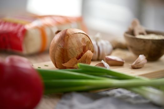 Close-up of fresh onions, garlic, and peppers on a rustic kitchen table, perfect for culinary themes.