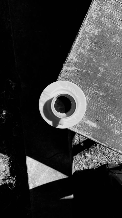 Free Artistic black and white shot of a coffee cup casting a shadow on a wooden table. Stock Photo