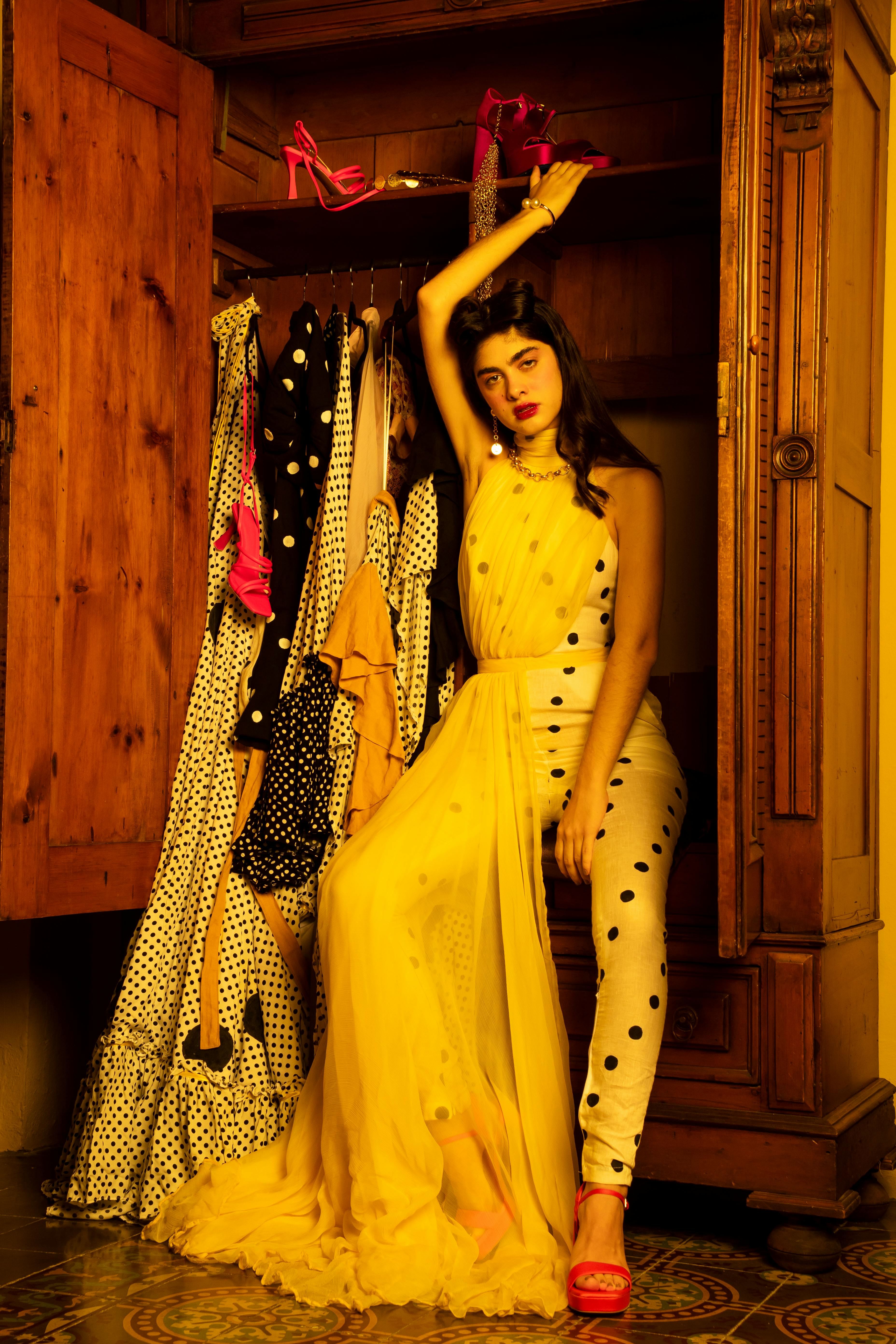 Stylish woman posing in yellow dress by wooden wardrobe showcasing fashion.