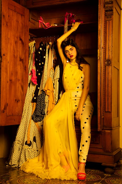 Woman in a Dress Sitting in an Opened Wooden Closet with Dresses Hanging on the Rack 