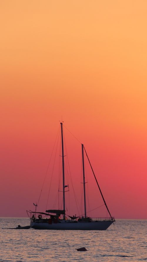 Free Serene image of a sailboat against a vivid sunset sky over the sea. Stock Photo
