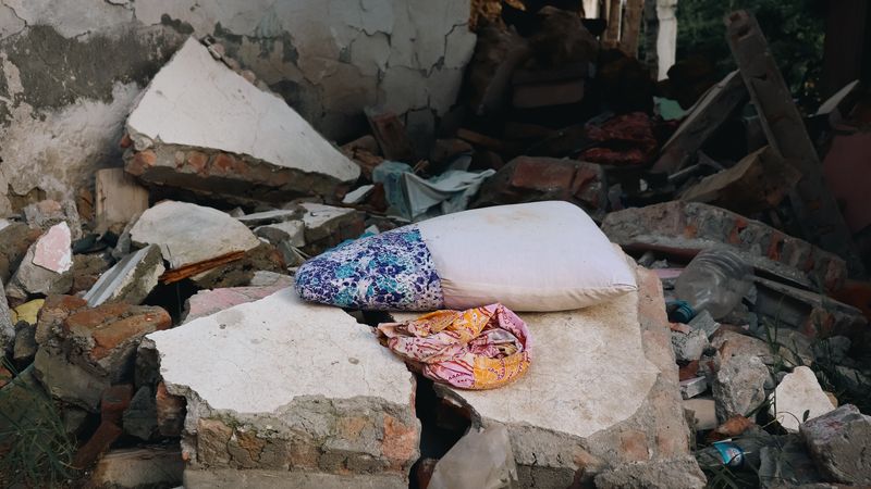 Urban earthquake aftermath showing destroyed buildings, rubble, and a pillow amidst debris, conveying devastation.