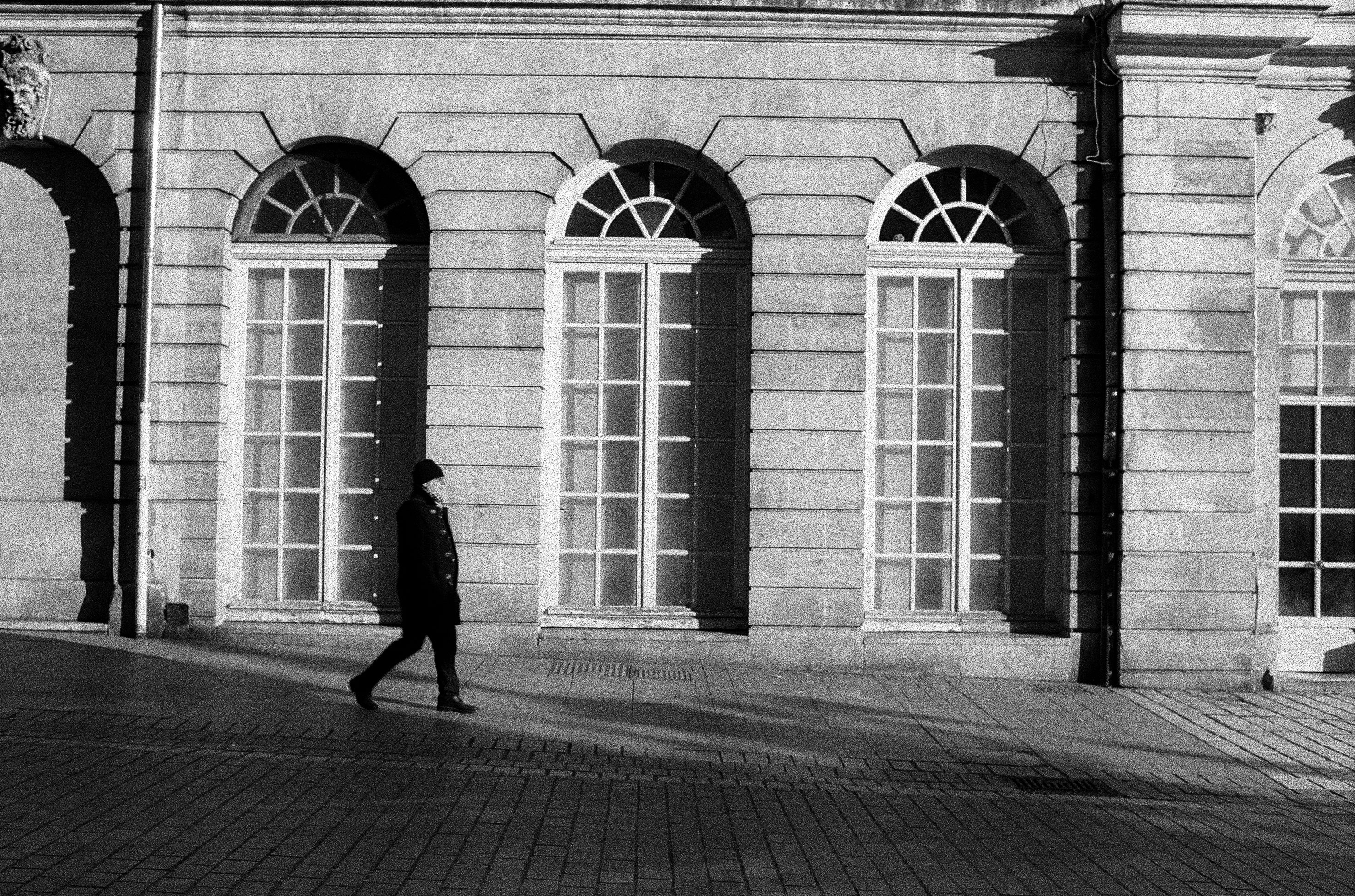 Black and White Picture of a Man Walking on the Sidewalk in front of a ...