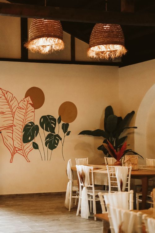 Free A beautifully designed restaurant interior featuring a unique plant mural, wicker lamps, and wooden furniture. Stock Photo