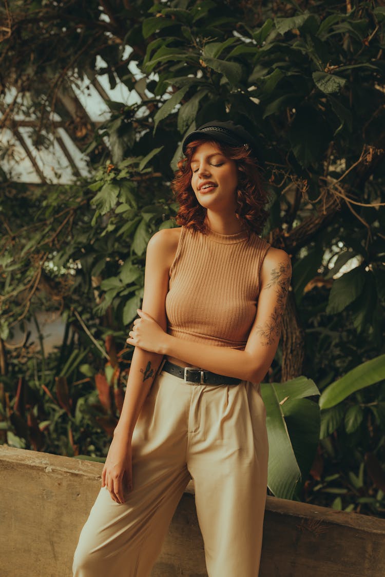 Young Woman In A Casual Summer Outfit Standing On The Background Of Green Plants