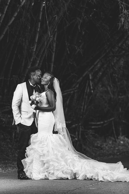 Black and White Photo of Groom Kissing Bride Wearing White Gown