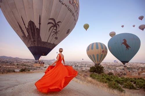 Woman in Red Gown Dancing in front of Flying Hot Air Balloons