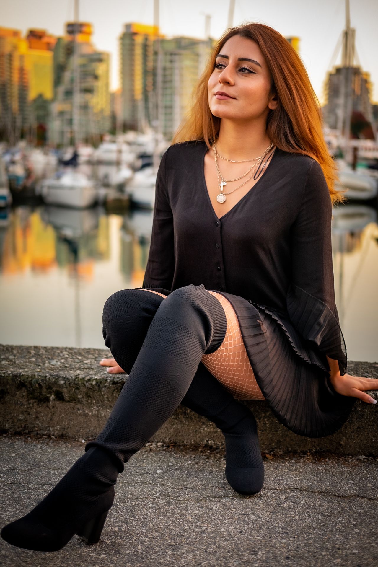 Woman in a black dress and black over-knee boots sitting by a marina