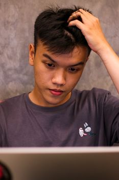 Portrait of a young man with short black hair, looking thoughtful while touching his head.