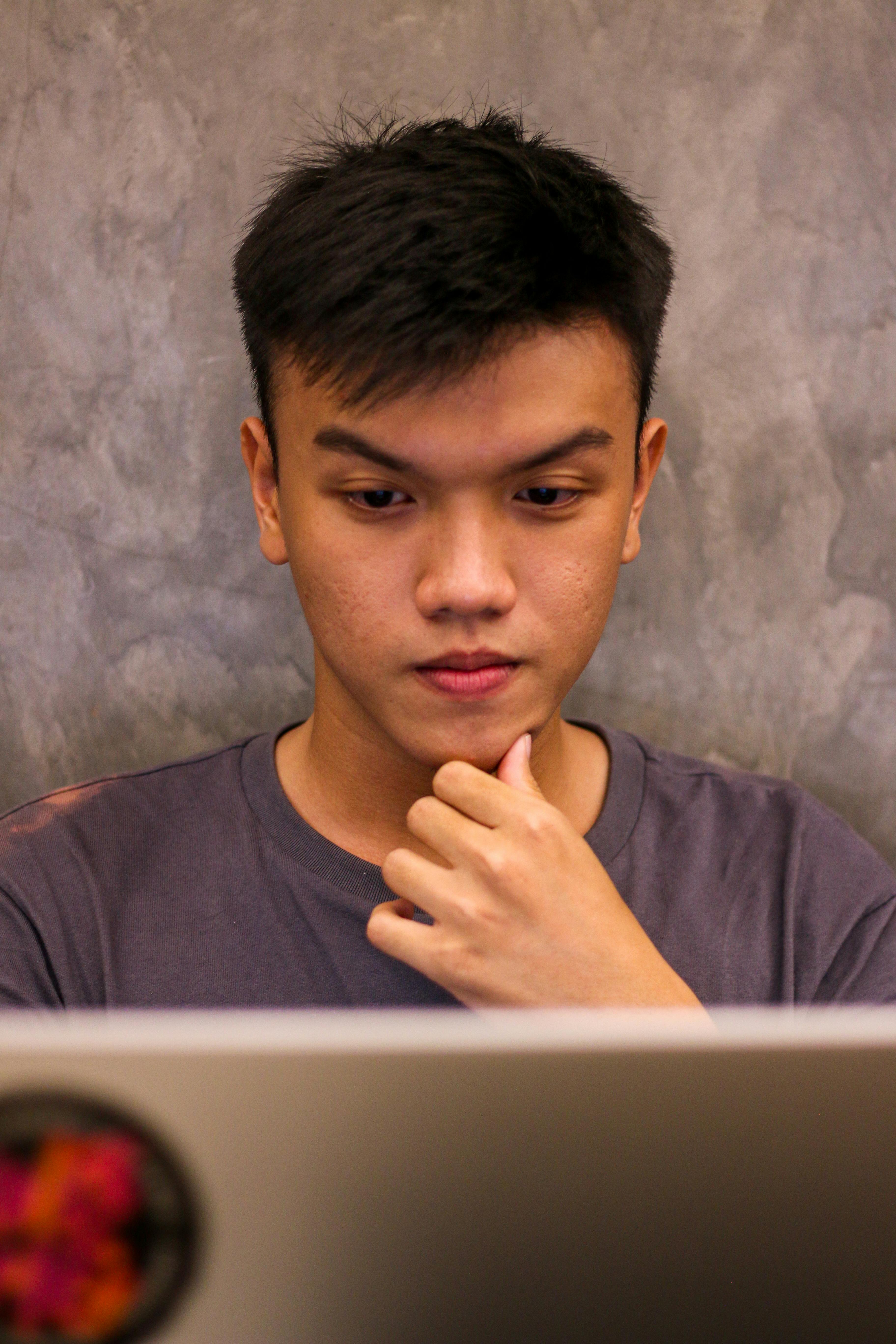 Asian man focused on using a laptop while indoors. Portrait shot highlighting concentration.