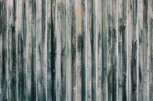 Texture of rusty metal surface with vertical stripes or slats and cracked paint in tones of green, white and yellow. Old weathered gate background with empty space for text