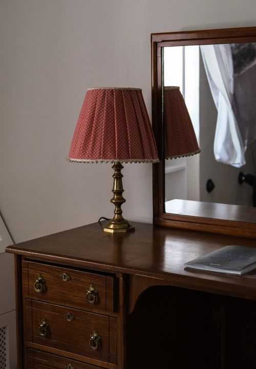 Free A vintage wooden dresser topped with a classic lamp beside a reflective mirror, offering elegant decor inspiration. Stock Photo