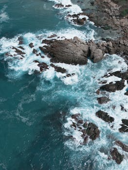 Stunning aerial view of turquoise waves crashing against rocky shore in Puerto Escondido, Mexico.