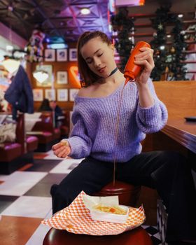 Young woman enjoying fries with ketchup in a colorful retro diner setting.