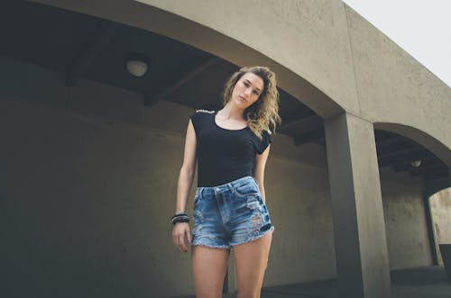 Young Woman in a Black Top and Denim Shorts Posing Outside
