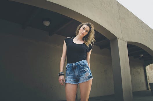 Stylish young woman in denim shorts and black top outdoors in summer.