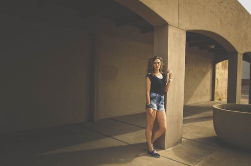 Pretty Woman in Black Top and Denim Shorts Posing by Column