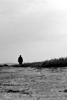 A solitary silhouette stands on a gravel path under an overcast sky, evoking solitude and mystery.