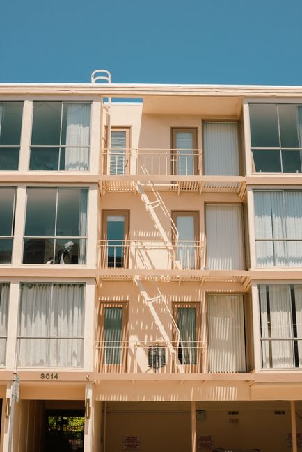 Contemporary building facade featuring balconies, large windows, and a fire escape under a clear blue sky.