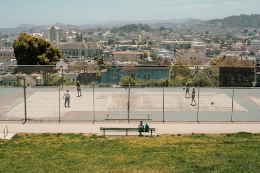 An aerial view of people playing basketball in a park with a cityscape backdrop, showcasing urban recreation.