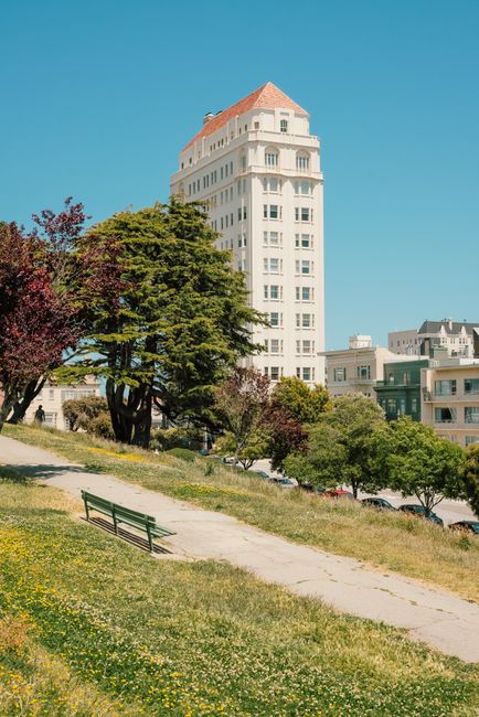 Idyllic park view with a bench and historic building under a clear sky, perfect for serene urban captures.