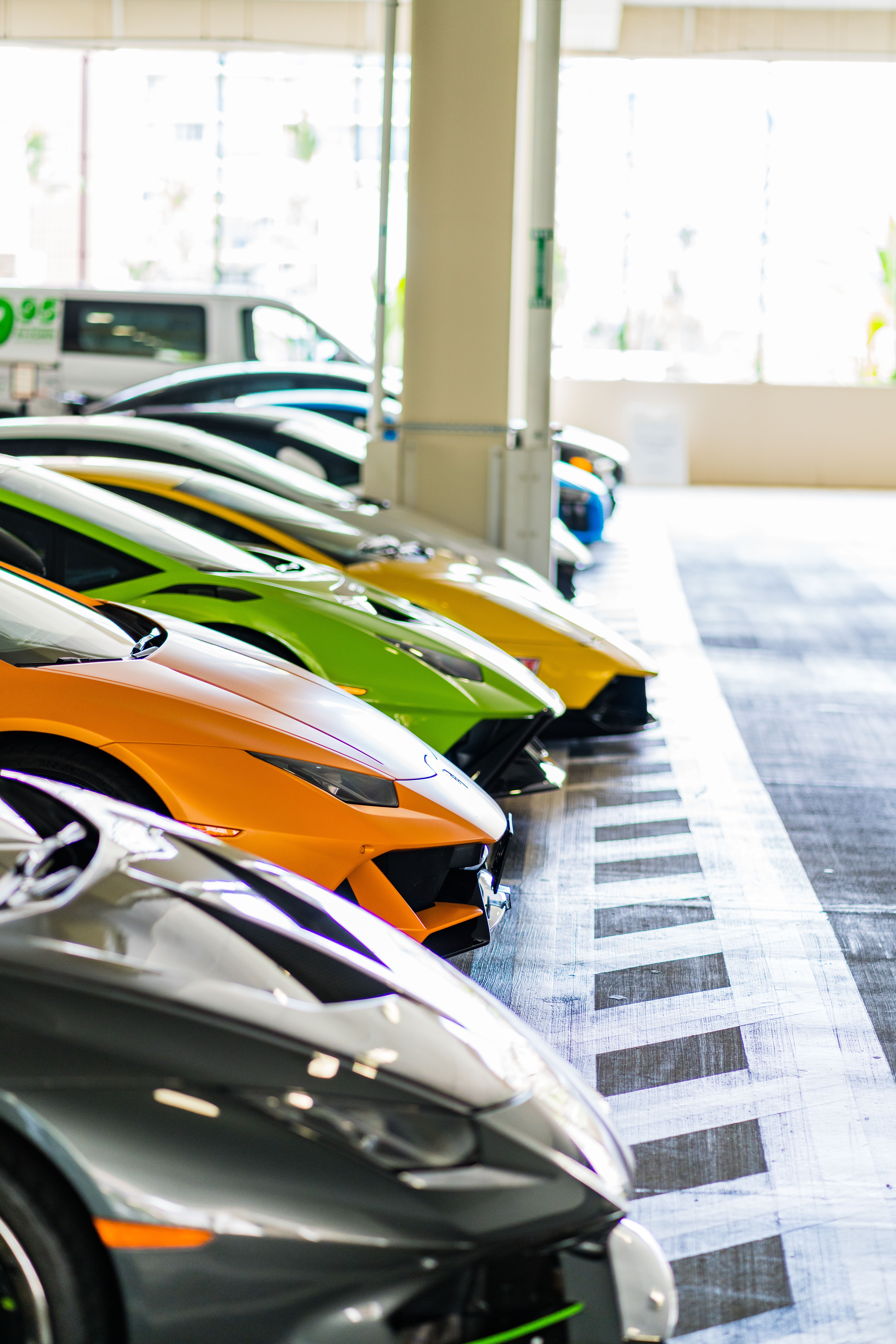 A lineup of colorful luxury sports cars parked indoors, showcasing sleek designs and vibrant colors.