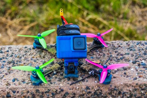 Free Colorful drone with camera positioned on a pebbled surface, ready for takeoff. Stock Photo