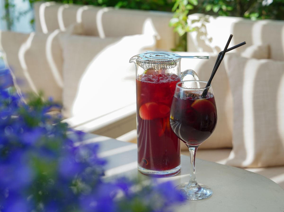Pitcher of red sangria with fruit and ice beside a wine glass on a sunny patio