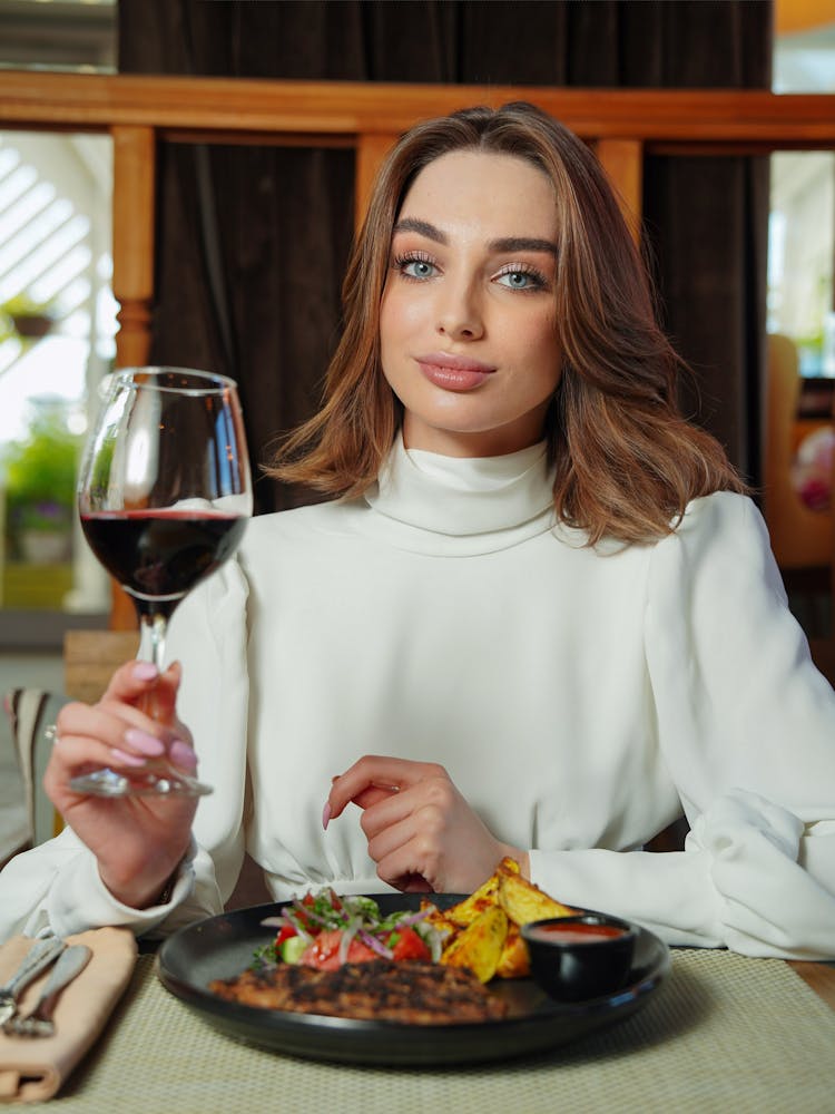 Young Woman Sitting At The Table In A Restaurant And Holding A Glass Of Red Wine