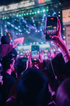 Energetic concert in Rome, Italy with vibrant lights and audience recording the show.