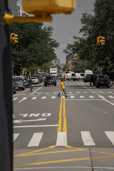 Pedestrian crossing a bustling New York City street with cars and traffic lights in view.