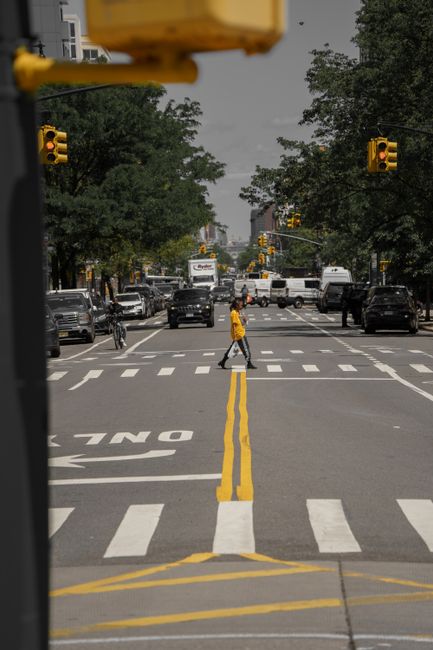 Pedestrian crossing a bustling New York City street with cars and traffic lights in view.