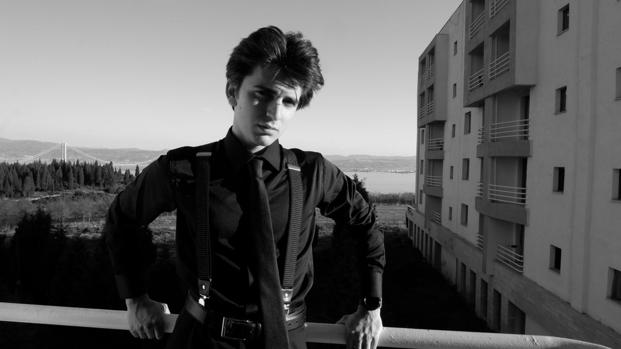 elegant monochrome portrait of a young man in suspenders on a balcony