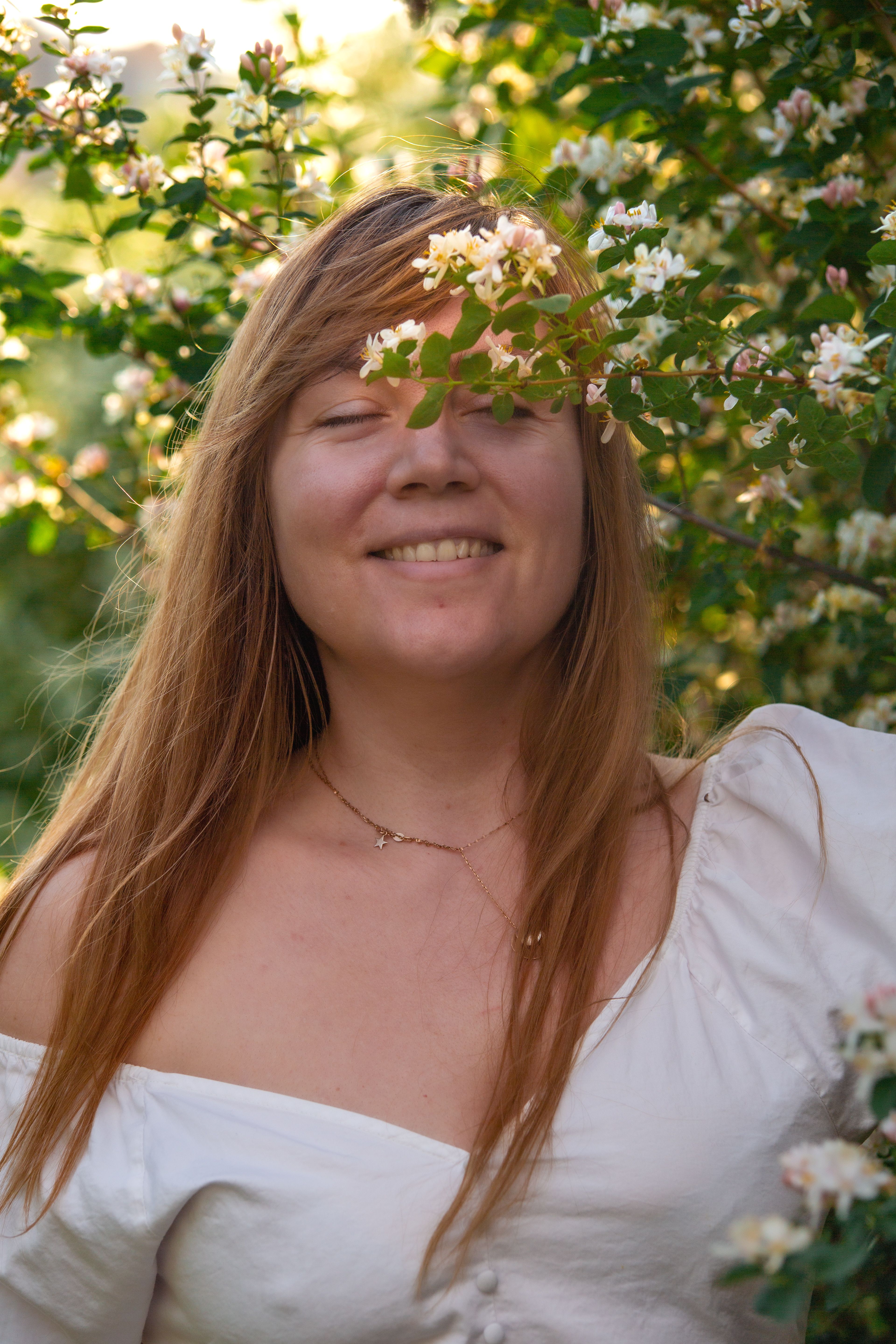 A woman in a white sundress enjoying a serene moment with blossoming flowers in spring.