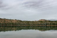 在多云的天空下，爱达荷州一座宁静的湖泊映照出周围的树木和山丘