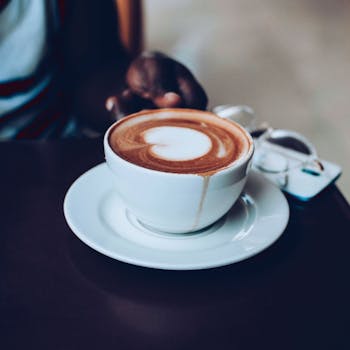 A delicious cappuccino with heart-shaped latte art served in a white cup on a saucer.