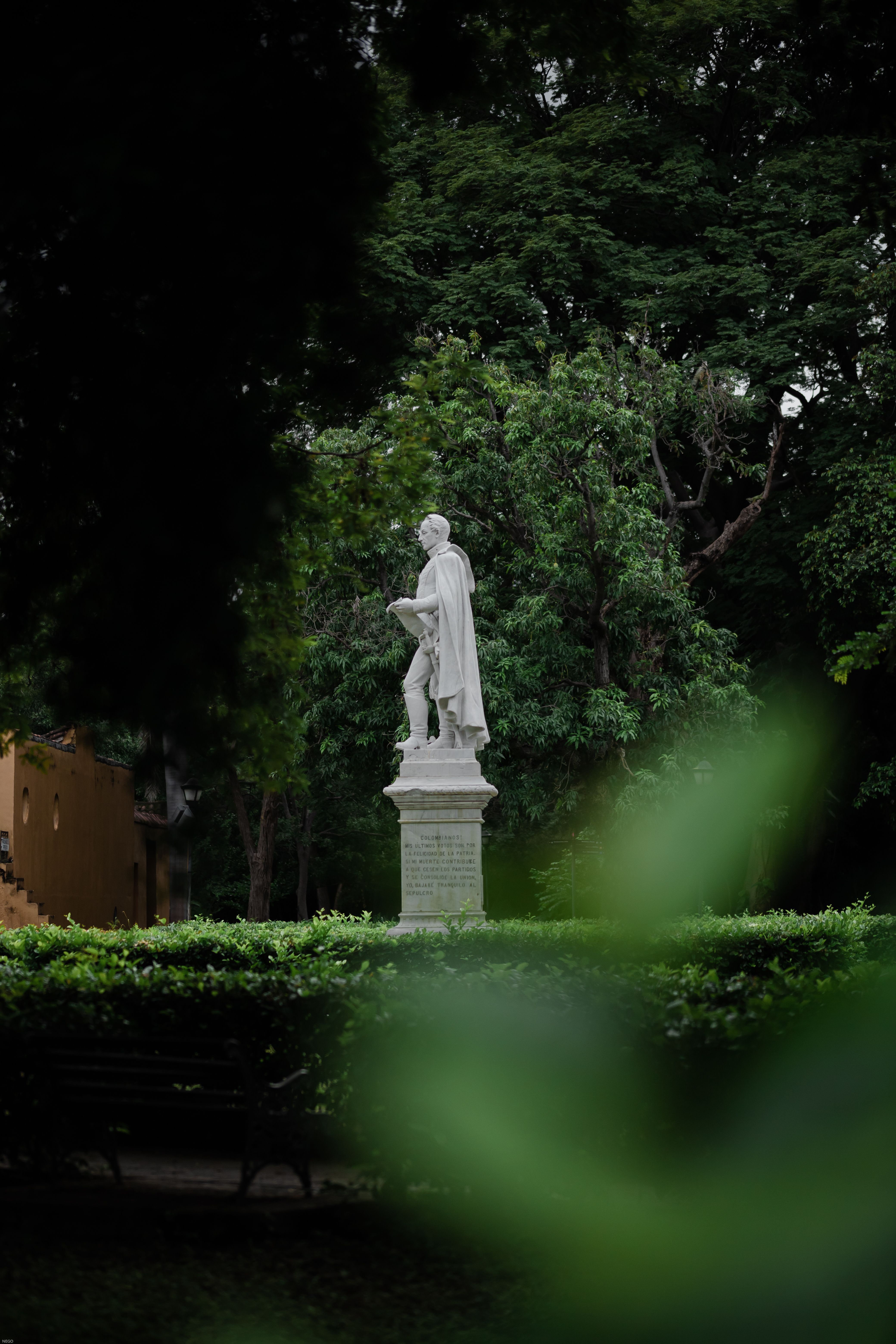 White marble statue surrounded by vibrant green foliage in a calm urban park setting.