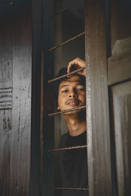 Free Portrait of a young man smiling through wooden bars on a window indoors. Stock Photo