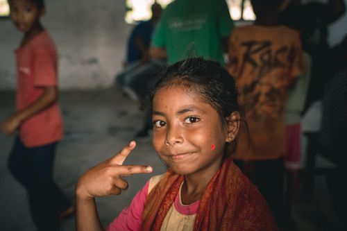 Free A young girl smiling while making a peace gesture in a lively indoor setting. Stock Photo