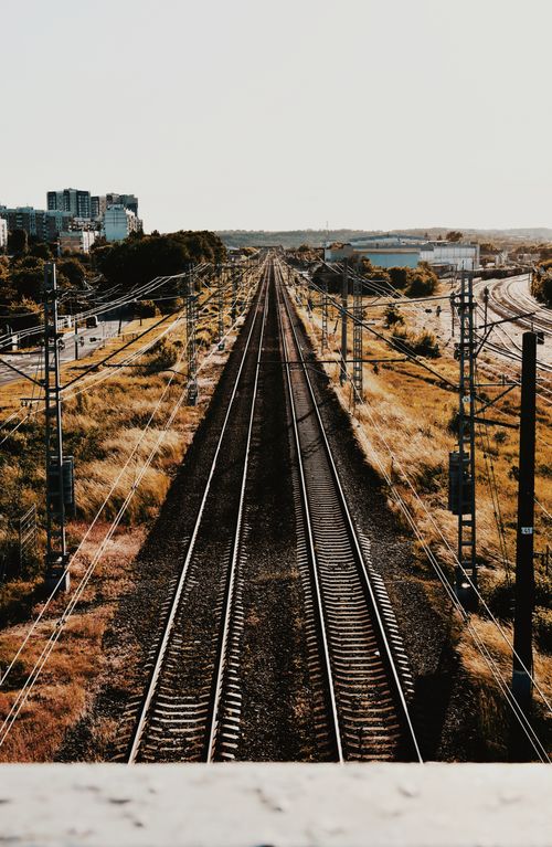 Free A perspective view of railway tracks extending towards a cityscape, captured during the day outdoors. Stock Photo
